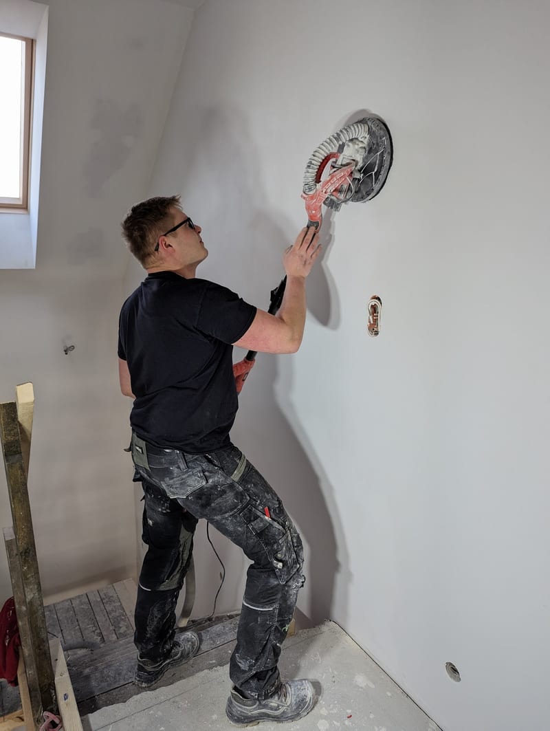 Jakub Kowalski — właściciel firmy Kowalski Remonty i Wykończenia — szlifuje ścianę żyrafą w trakcie remontu